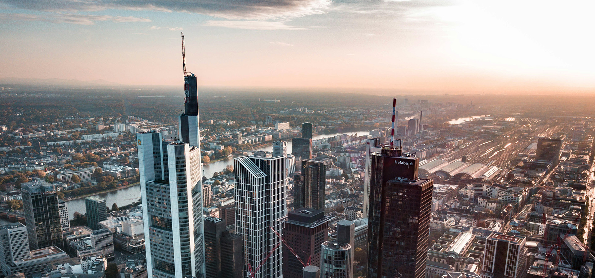 Luftaufnahme einer modernen Stadtlandschaft bei Sonnenuntergang mit prominenten Wolkenkratzern, einem Fluss und urbaner Infrastruktur — spiegelt den Fokus von ENIGMA GmbH auf Immobilieninvestments und Stadtentwicklung wider.