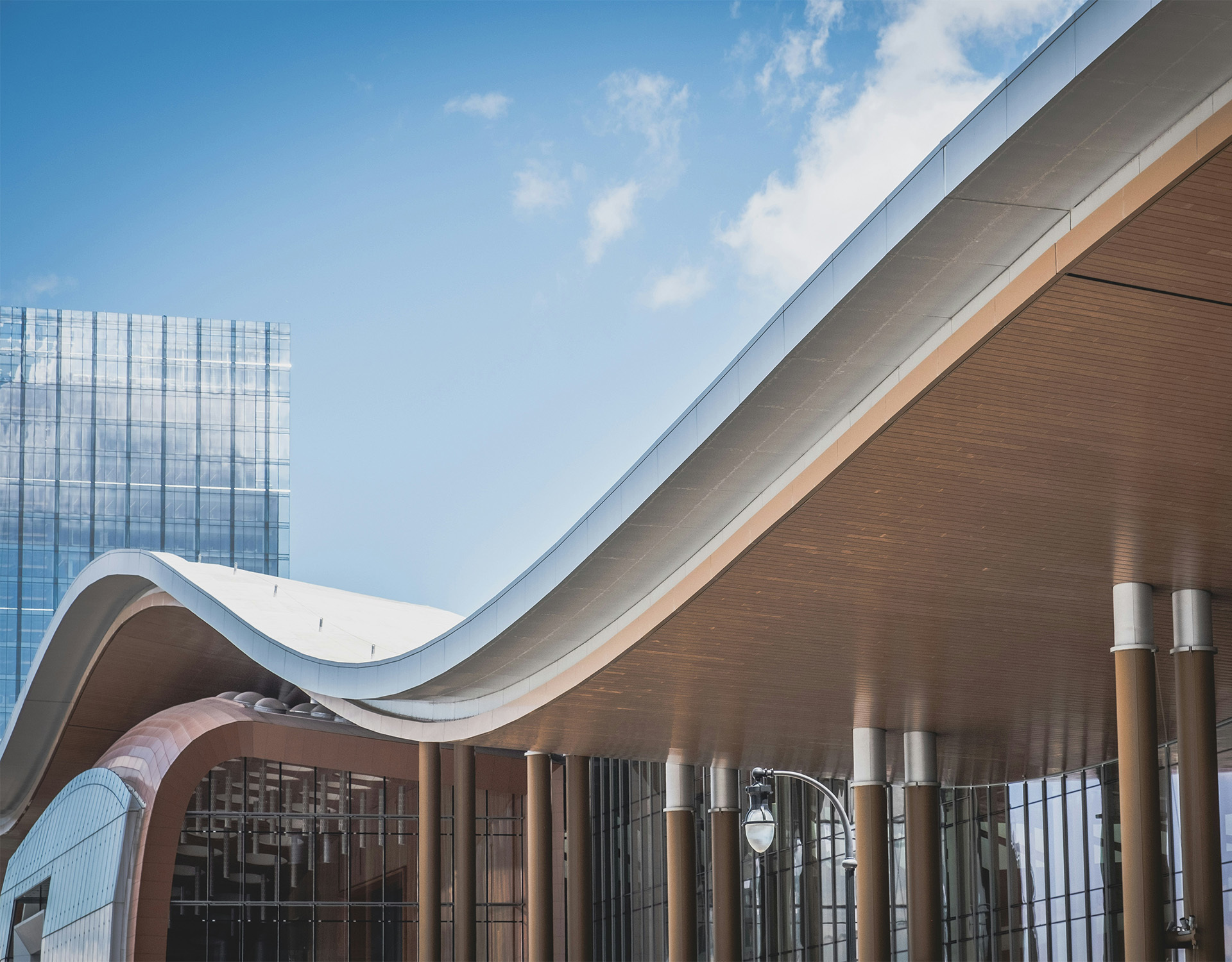 Moderne Gebäudearchitektur mit einem gewölbten Dach, Glasfassade und einem hohen Glasgebäude im Hintergrund unter klarem blauem Himmel.