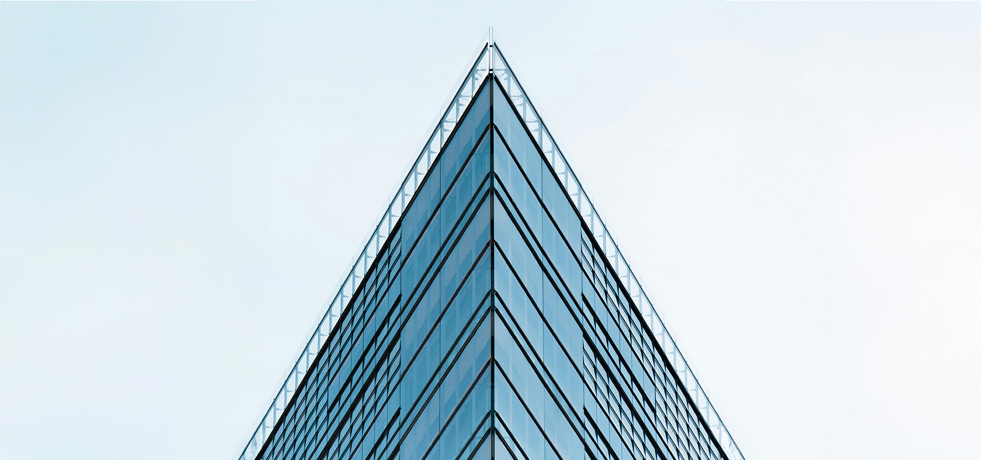 Spitzes, modernes Hochhaus mit blauer Glasfassade gegen einen hellen Himmel – symbolisch für die zukunftsorientierte Immobilien- und Investmentstrategie von ENIGMA GmbH.