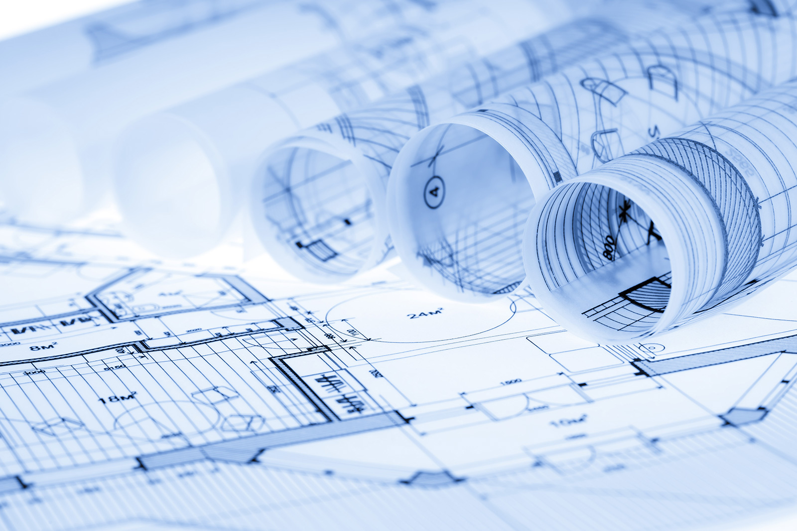 Architektonische Baupläne und Rollen von technischen Zeichnungen, die die Wertschöpfung in Immobilienprojekten symbolisieren – ein zentrales Thema für ENIGMA GmbH, ein Consulting- und Investmentunternehmen mit Fokus auf Immobilieninvestments.